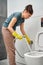 A woman in yellow rubber gloves flushes the toilet bowl with a hygienic watering can.