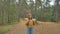 Woman in yellow sweater with backpack poses in pine forest