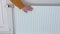 A woman in a yellow sweater checks the heat in the radiator heater in her apartment with her hands. The concept of the