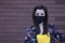 Woman in yellow t-shirt and flowery shorts costume. In black face mask. brown wall background. modern reality