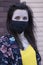 Woman in yellow t-shirt and flowery shorts costume. In black face mask. brown wall background. modern reality