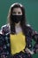 Woman in yellow t-shirt and flowery shorts costume. In face mask.modern reality. green wall background. covid-19 concept