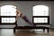 A woman yoga instructor trains on a reformed Cadillac in a large hall against a window, modern equipment for training in