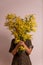 Womans day mimosa. vertical portrait of young woman holding yellow heart shaped mimosa flowers bouquet on white background smiling