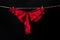 Womans erotic red underwear panties hanging on rope isolated on black background. Lace lingerie, woman sexy underwear.