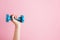 Womans hand holding blue dumbbell isolated on pink background. Equipment for home workout. Fitness and activity. Sport and healthy