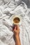 Womans hand holding a cup of coffee on the bed with white linen on the room with natural sunlight