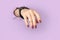 Womans hand with purple matte manicure through hole in paper background