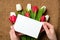 Womans hands holding a card with copy space for text above burlap canvas with tulips flowers. Greeting card for International Woma