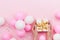 Womans hands holding gift or present box on pink pastel table decorated balloons and confetti. Flat lay composition.