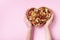 Womans hands holding heart shaped bowl with mixed nuts on pink table top view. Healthy food and snack. Flat lay