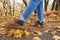 Womans leg kicks yellow autumn leaves from the ground in the park