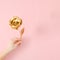 Womanâ€™s hand holding golden rose on pastel pink background with copy space. Top view.