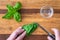 Womanâ€™s hands chopping fresh basil with a paring knife on a rustic grove bamboo cutting board, small glass bowl