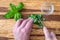 Womanâ€™s hands chopping fresh basil with a paring knife on a rustic grove bamboo cutting board, small glass bowl