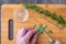 Womanâ€™s hands chopping fresh sprig of rosemary with a paring knife on a bamboo cutting board, small glass bowl