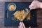 Womanâ€™s hands holding chef knife and chopping walnuts, black cutting board, glass bowl, dark wood table