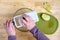 Womanâ€™s hands using a mandolin slicer on a granny smith apple, cutting board, and glass bowl on a butcher block table