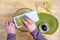 Womanâ€™s hands using a mandolin slicer on a granny smith apple, cutting board, and glass bowl on a butcher block table