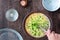 Womanâ€™s hands whisking raw egg mixture with chopped broccoli in glass bowl, on a wood table