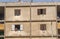 Women in colorful head scarves laugh out cement apartment window as a small boy looks down at them from above