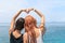 Women couple forming heart shape with arms at the sea