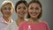 Women of different age with pink ribbon smiling at camera, breast cancer control