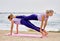 Women do partner yoga make Double Plank pose near sea