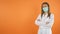 Women doctor with face mask smiles in front of the camera.Orange studio background Copy Space concept