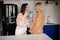 Women drinking tea standing in kitchen together. Brunette smiling while keeping hand on tummy of pregnant happy blonde.