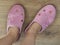 Women feet are shod in a home pink slippers. Cozy, warm and comfortable domestic shoes. On a brown wooden floor