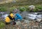 Women Filling Water Bottles at Creek