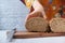 Women hand cutting baked brow bread on table.