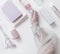 Women hand holding pink  cosmetic bottle on modern beauty  background with packaging boxes, candles and flowers. Top view. Pastel