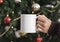 Women hand holding white ceramic coffee cup with christmas tree background. mockup mug for creative advertising text message