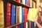 Women hand pulling yellow book from wood bookshelves in public library. Colorful books, Textbook, Literature on bookshelf.