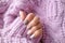 Women is hands with a beautiful matte oval manicure in a warm purple knitted sweater. Winter trend, polish beige nails with gel