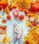 Women hands holding bottles of cosmetic products on white blanket with pumpkins, candles and fall leaves. Autumn beauty concept.