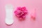 Women intimate hygiene products, sanitary pad, reusable silicone menstrual cup and beautiful fresh peony flower on pink background