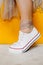 Women legs in white clean new sneakers, transparent thin socks with silver shiny stars and lush tulle dress on yellow background.