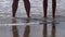 Women and man, couple with barefoot standing on the sand by the sea, wave crashing into her feet