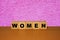Women message sign on a wooden desk on cube blocks with a pink abstract background.