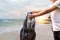 Women pick up trash on the beach, put in recyclable trash with beautiful sea backdrop.