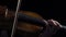 Women play strings of a violin in a dark room. Black background. Close up