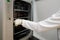 The women researcher with long sleeve shirt and gloves pickup tube and equipment from the cabinet to do the lab test.