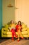 women in retro clothing reading books sitting on yellow sofa at bright apartment doll