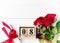 Women`s day background. 8 march wooden calendar, red roses, gift with red ribbon on the wight wooden background. Copy space, flat