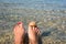 Women`s feet with a pedicure, which are immersed in the water on the beach. There is a starfish and a shell on the big toes