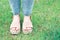 Women`s foot in summer brown sandals against background of green grass, copy space.