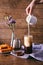 Women`s hand with creamer pouring milk in glass with coffee. Cinnamon sticks, homemade cookies and bunch of wildflowers
